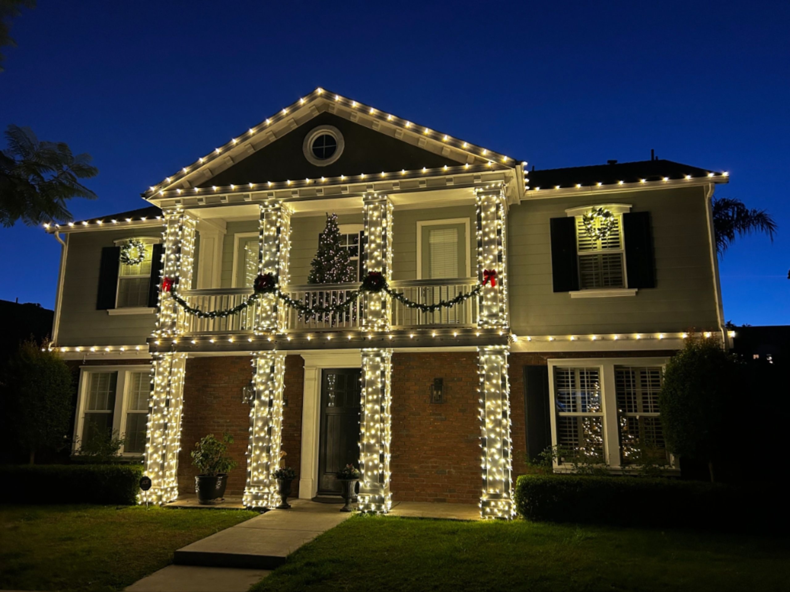 Two-story home decorated with warm white string lights and holiday wreaths at twilight
